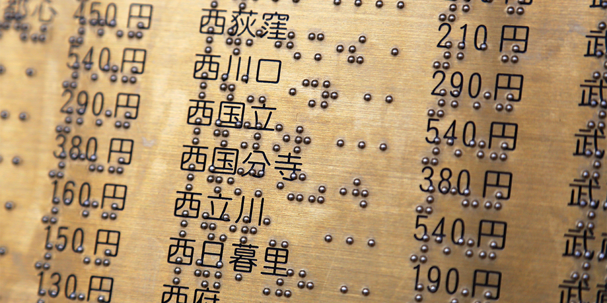 An engraved brass plate is shown with Arabic numbers, Japanese translation, and braille accompanying each.