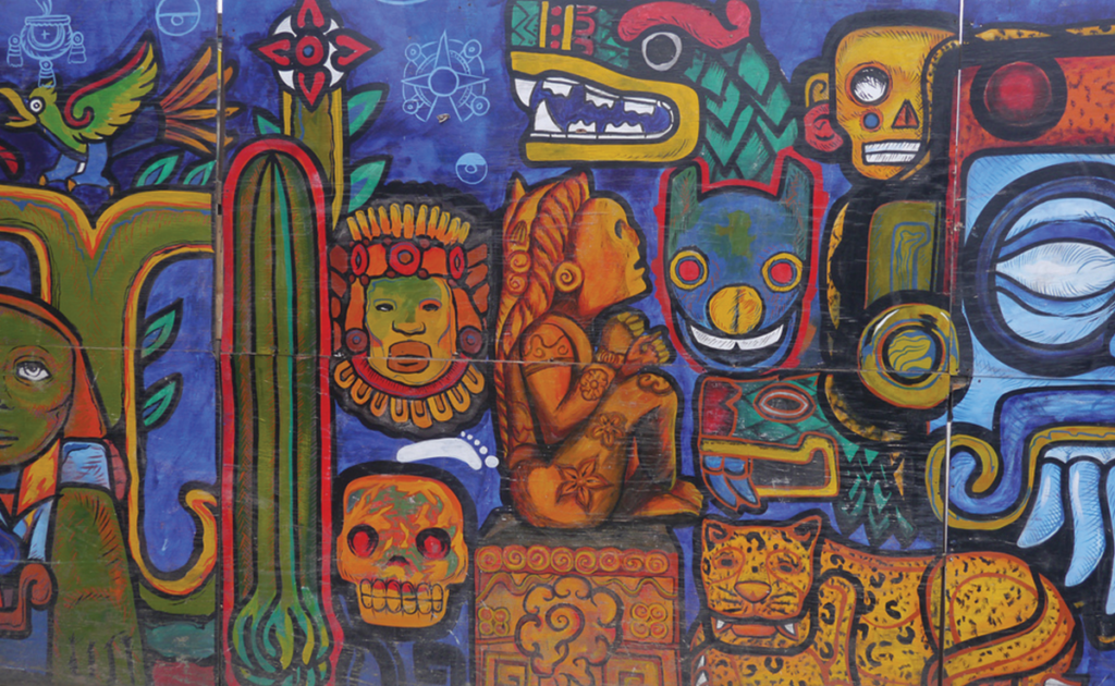 Graffiti in Mexico City features vibrant colors, primarily blues, greens, reds, and oranges with thick black outlines defining the shapes. Shapes include skulls, cactus, birds, jungle cats, statues, and masks.