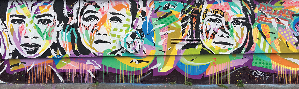 Mur Rue Alibert, by Jo Di Bona. A backdrop of bright, classic graffiti shapes, paint drips intermingling the colors, is overlaid by three separate black and white printed faces. The printed faces of a woman and two young girls have sections torn out, revealing the bright colors and shapes behind them.