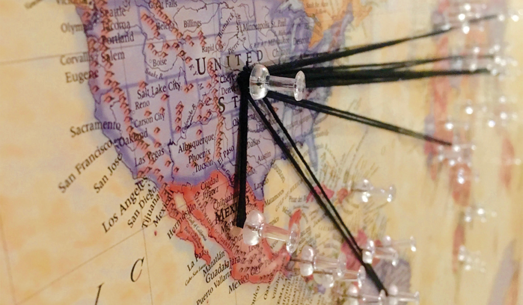 A map of the world, with the United States in the foreground, uses thumb tacks and yarn to represent the concept of global immigration to the US.