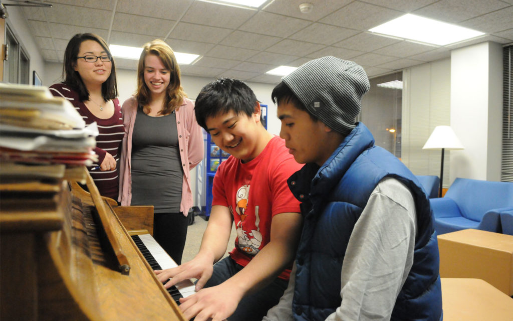 Students play the piano in the Scott Hall common area